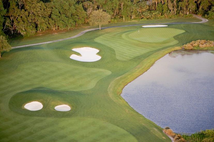 Aerial view of a winding fairway leading to a manicured green strategically placed next to a sand bunker and water hazard