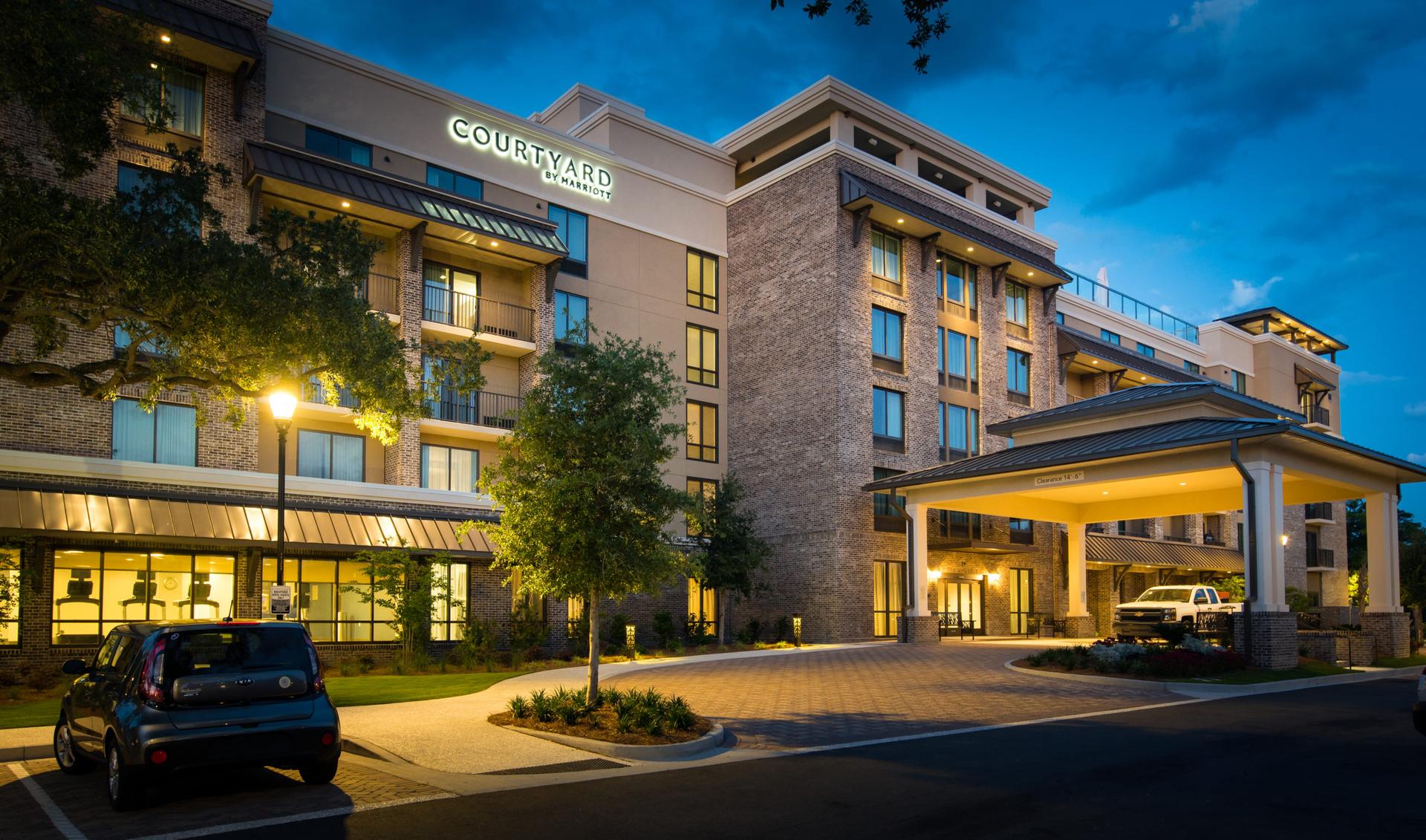 Exterior view of the Courtyard hotel with its sign illuminated at the top of the building parking and drop off area