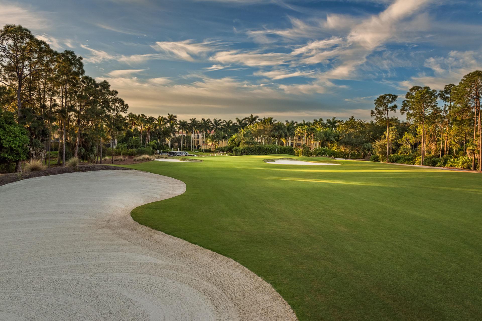 A lush fairway bordered by trees and elegant sand bunkers.