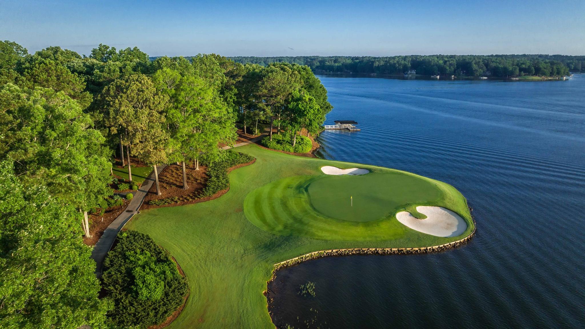 A lakeside green surrounded by sand traps, framed by trees and calm water.