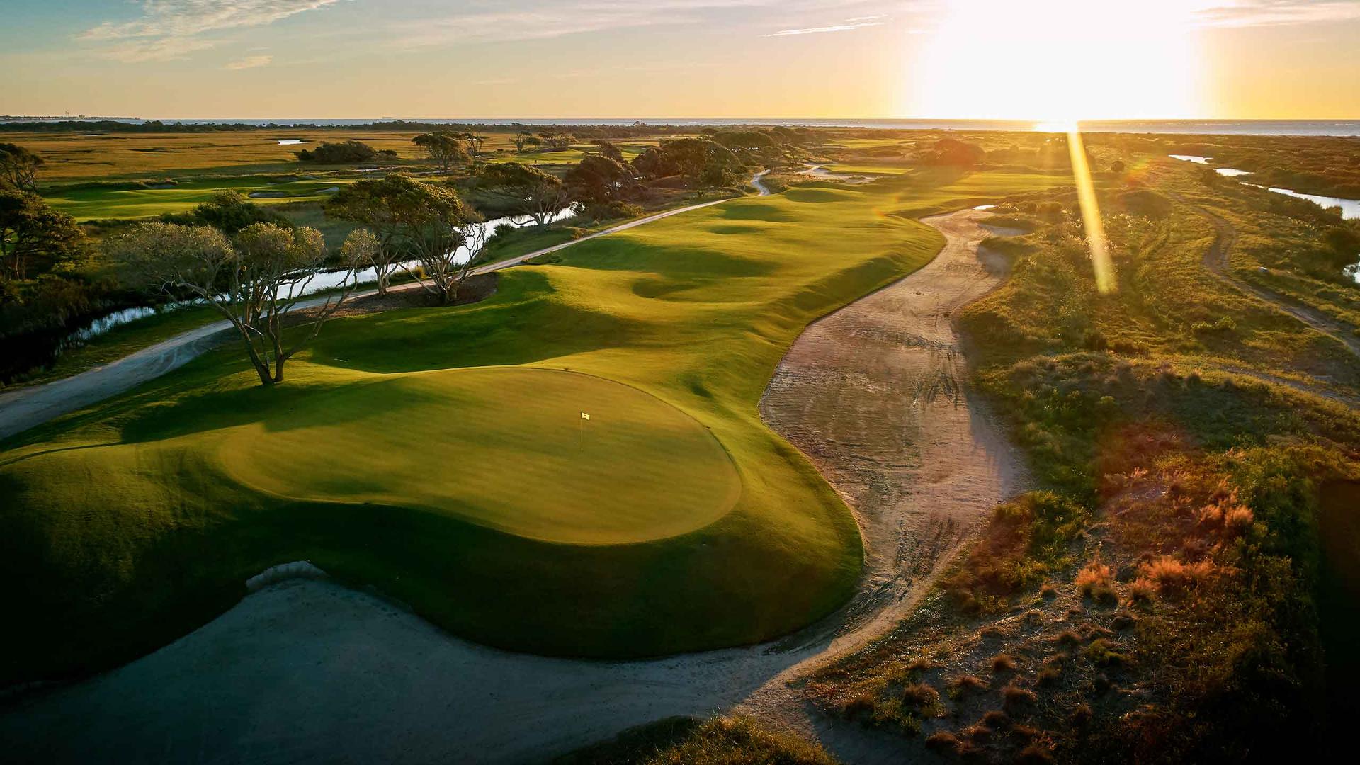 A dramatic golf course hole illuminated by the golden light of the setting sun.
