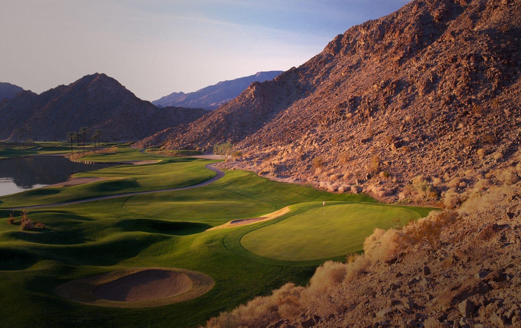 Smooth green and rolling dunes sandwiched between a large water hazard and mountains