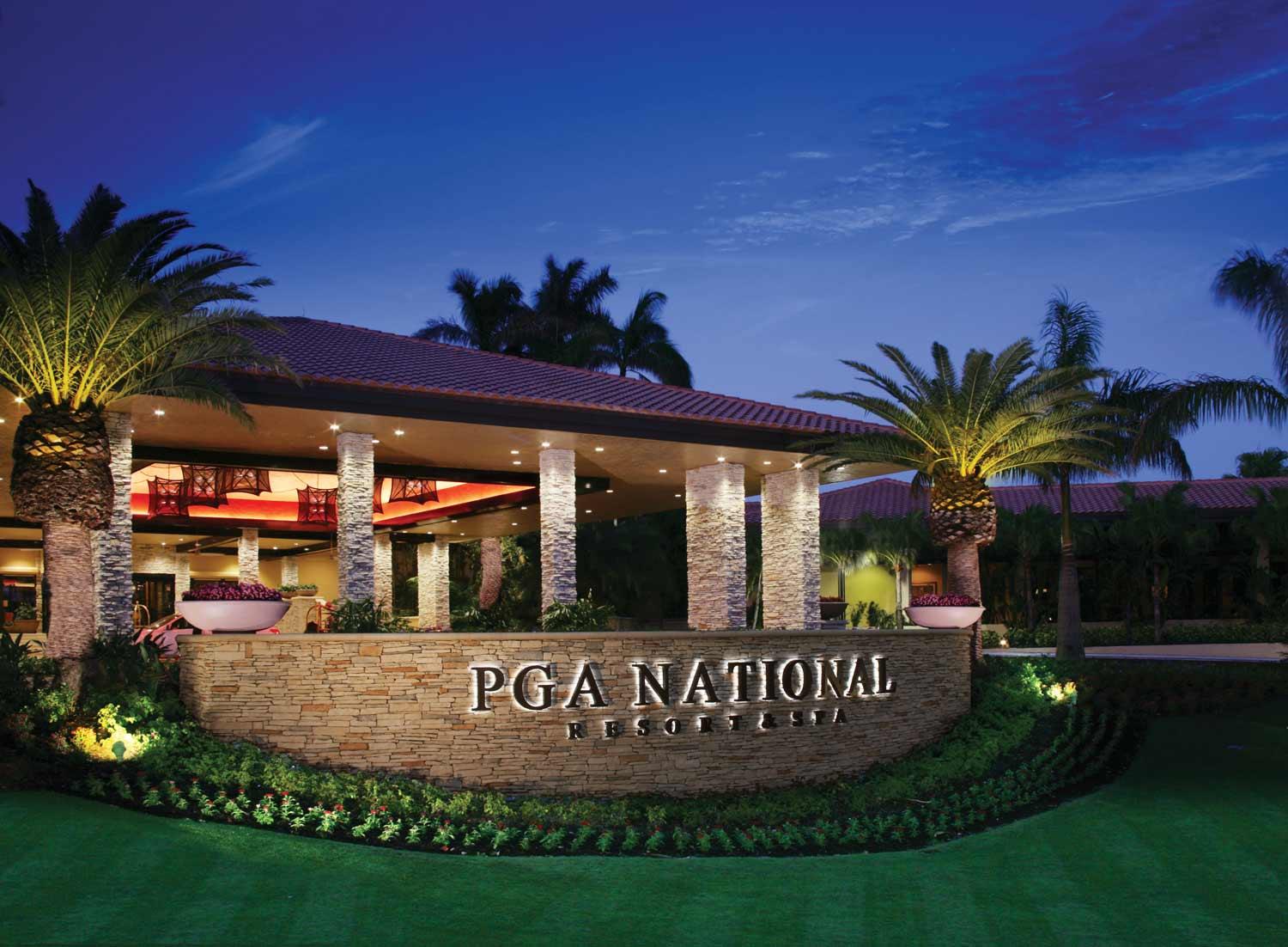 Front entrance to the resort with their illuminated sign surrounded by flowers and palm trees