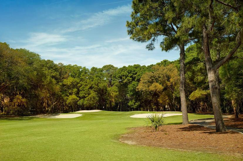 A wide fairway stretches toward sand bunkers and dense trees.