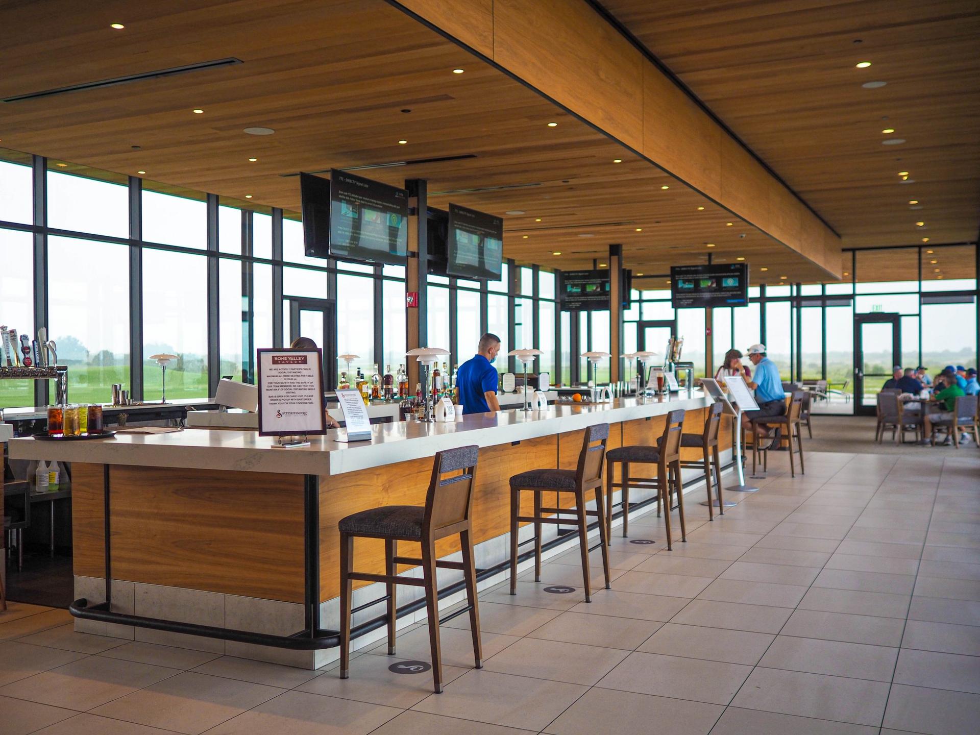 Modern bar at the resort equipped with multiple TV's around the bar and panoramic windows facing the course