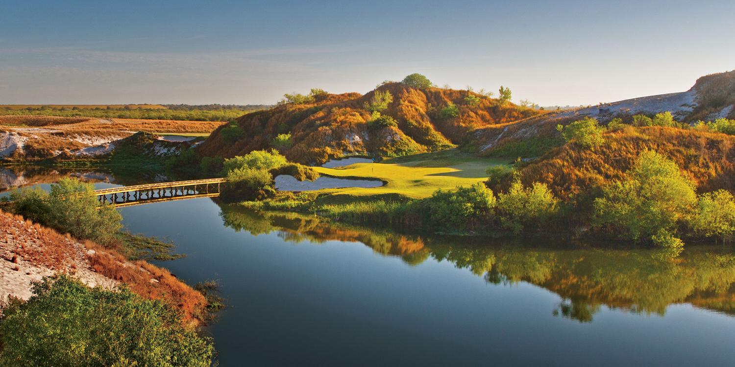Smooth green placed between mountains with a bridge over the lake to navigate the course