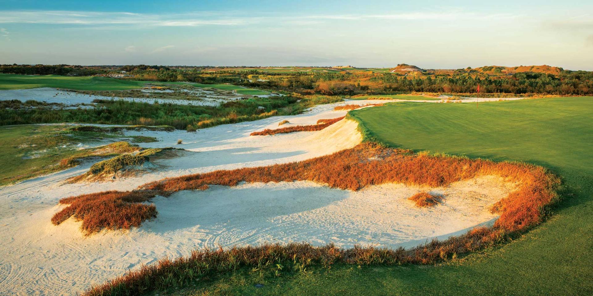Large sand bunker surrounding an elevated green under blue skies