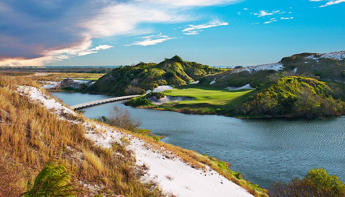 Smooth green placed between mountains with a bridge over the lake to navigate the course