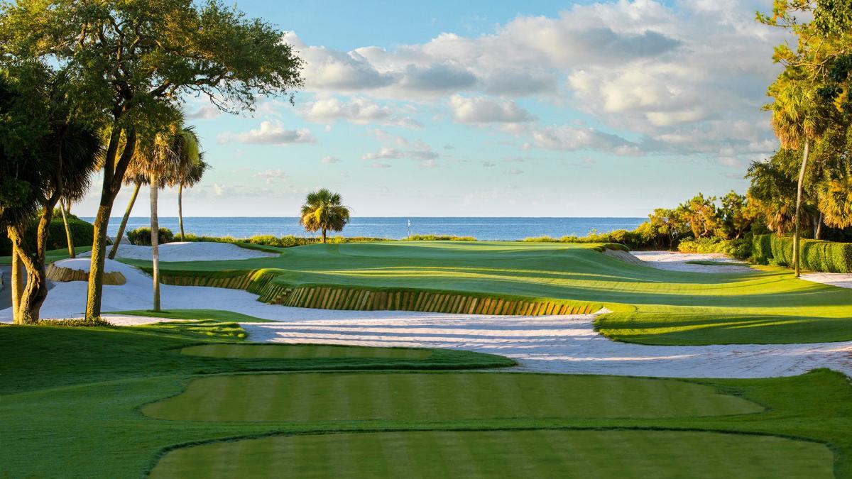 Fairway leading to a green with sea views elevated from a large sand bunker with a mood wall