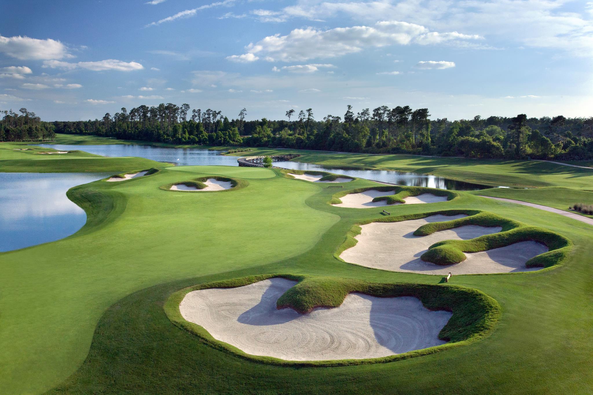 Expansive fairways lined with water hazards and intricate sand bunkers under a clear sky.