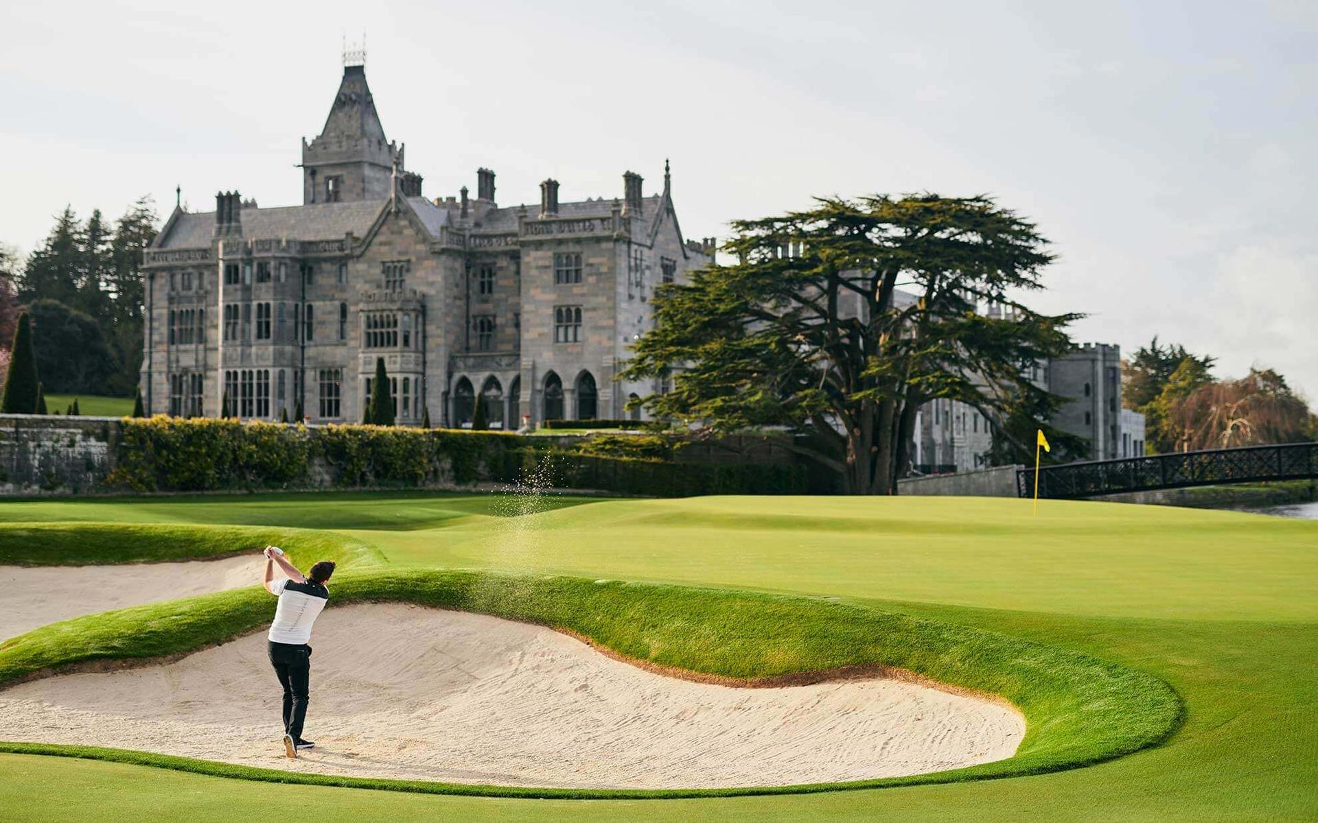 A golfer escapes a deep bunker near the iconic manor.