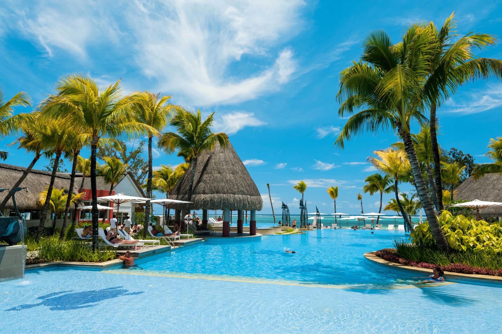 Outdoor swimming pool at the Ambre Resort & Spa surrounded by palm trees and sun beds