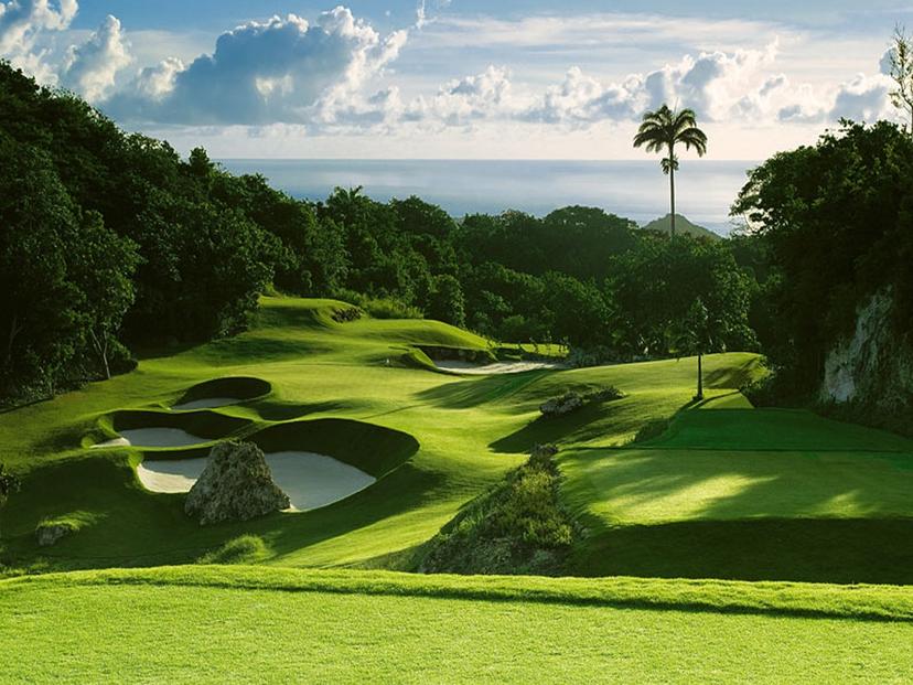 A winding downhill fairway nestled with large sand bunkers with sea views in the distance