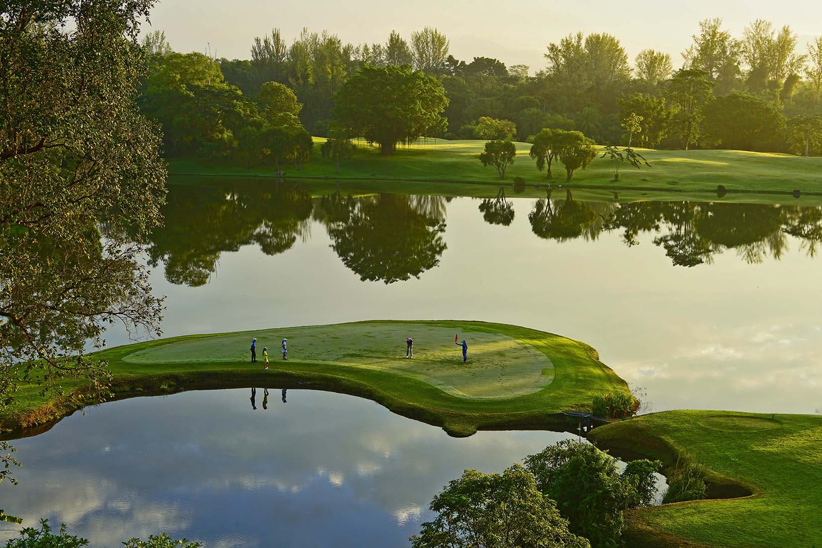 Golfers putting on an island green surrounded by water at sun set