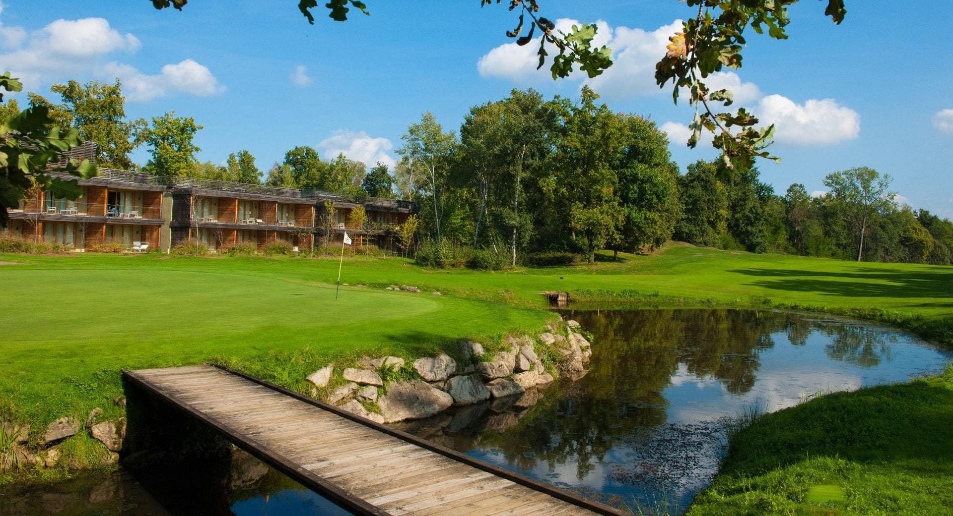 A charming wooden lodge next to a reflective pond and golf green.