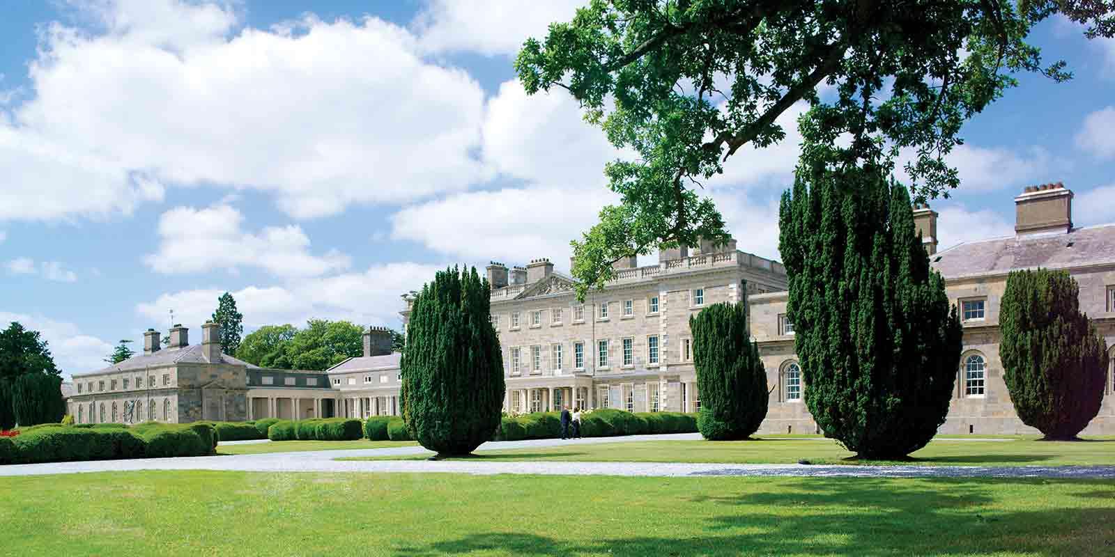 A stately manor house surrounded by perfectly manicured lawns and tall trees.