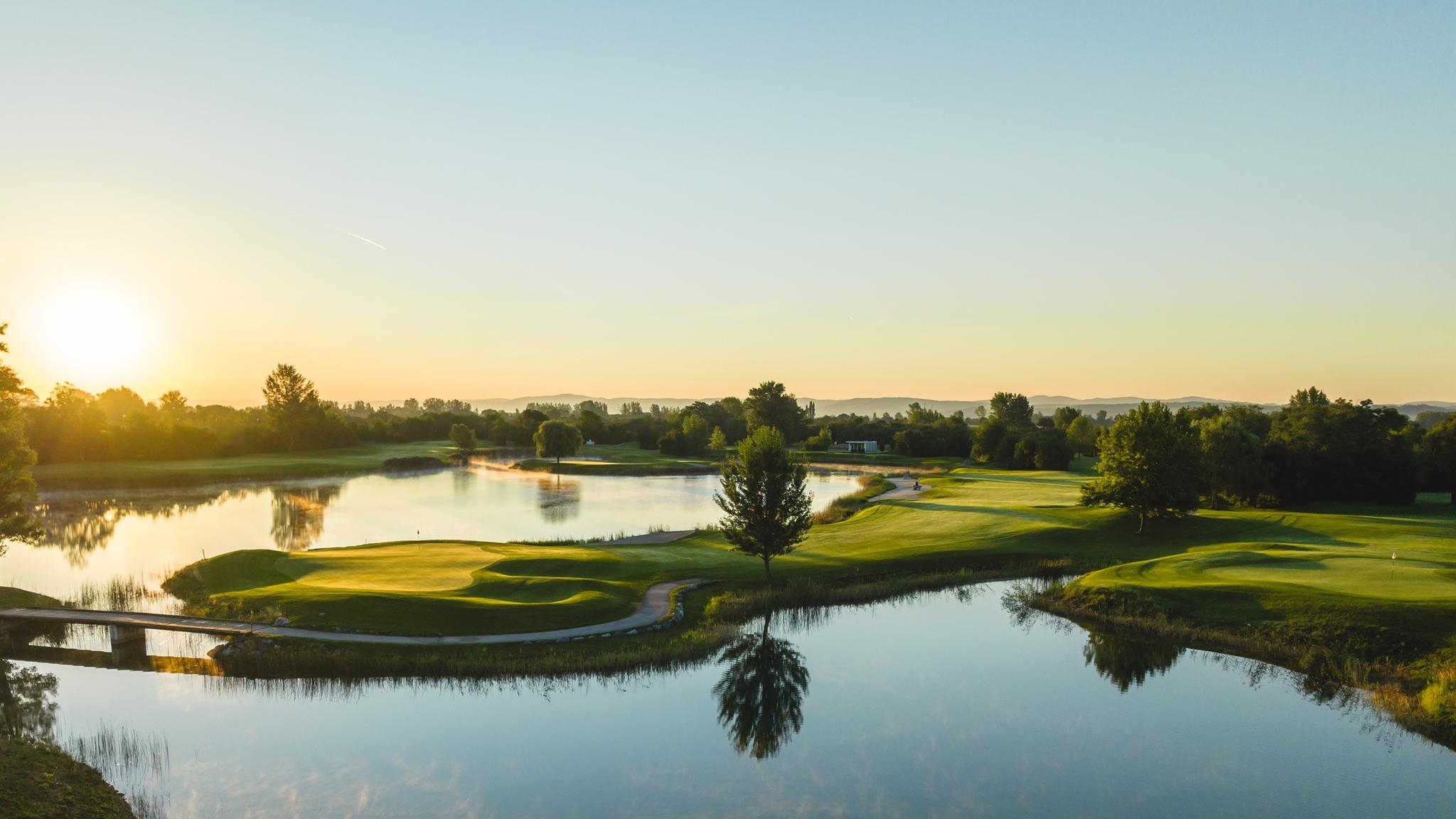 Sun setting over an island like green with a well-maintained fairway leading to it