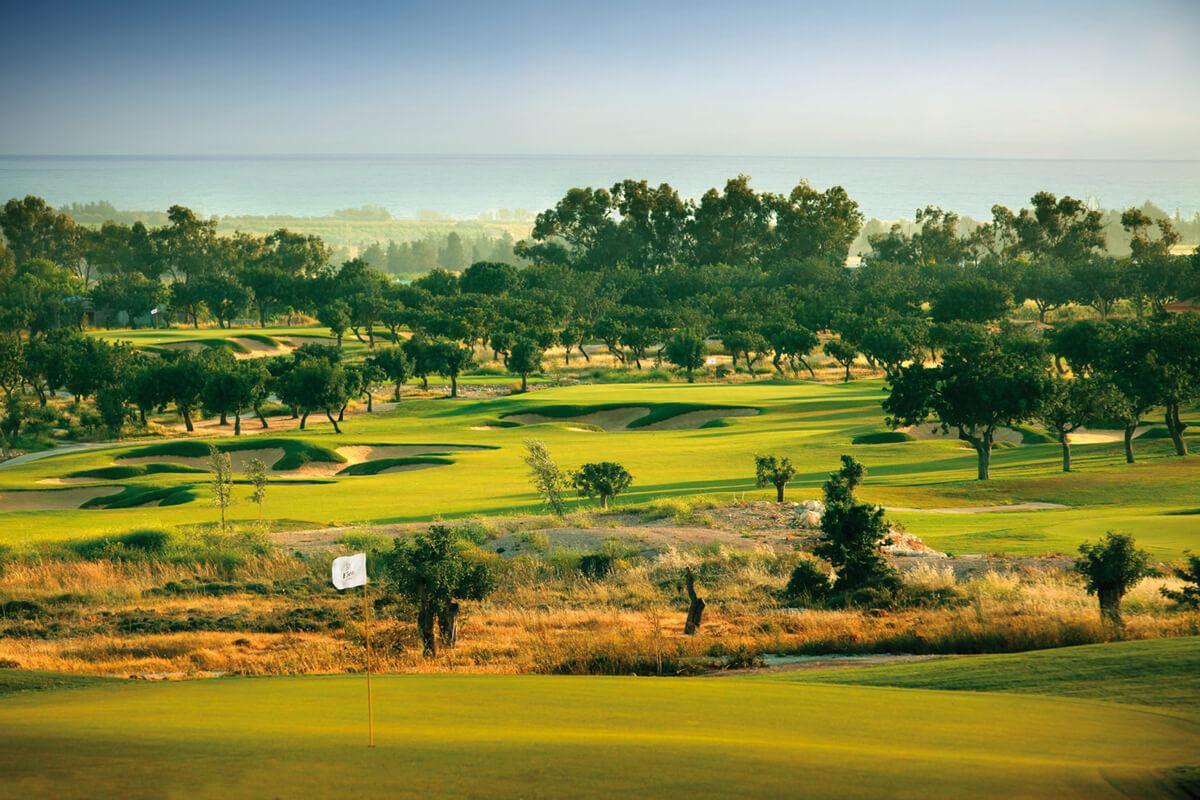 Lush fairways stretch towards the ocean, dotted with trees.