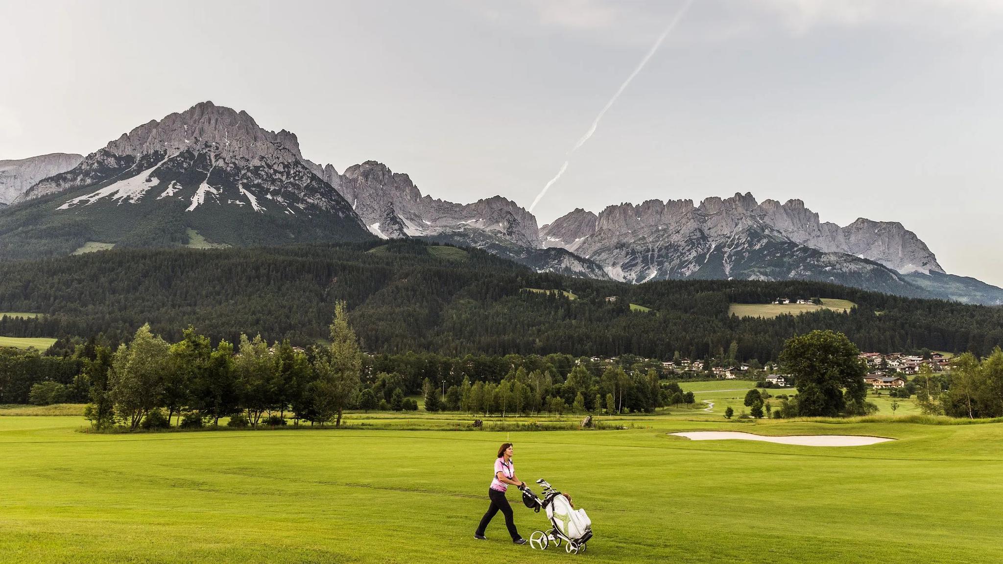 A well maintained fairway nestled with a single sand bunker and mountains towering over in the back