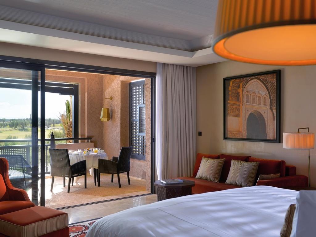A double bed room with sofas leading to a balcony with a dining area and landscape views