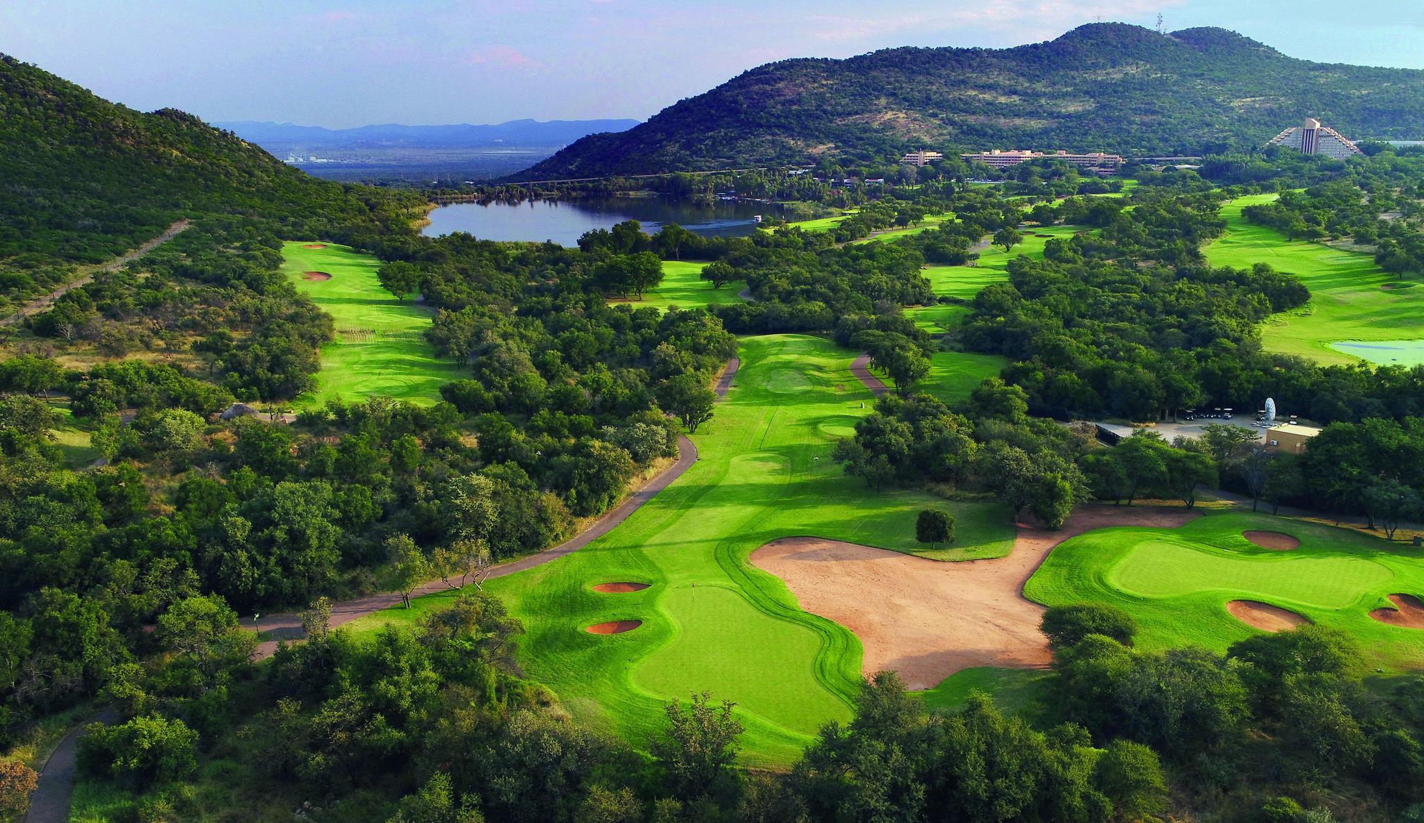 A golf course with lush fairways surrounded by dense trees and hills.