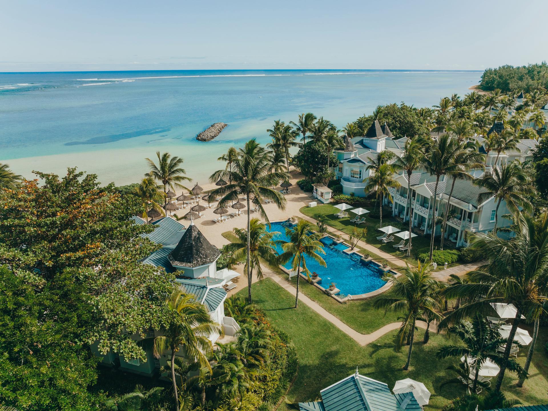Birdseye view of the outdoor swimming pool leading to the beach under clear blue skies