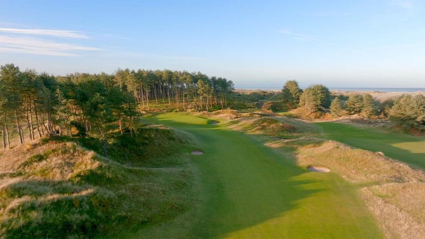 Overhead view of the fairway nestled with bunkers leading to the green with sea views in the distance