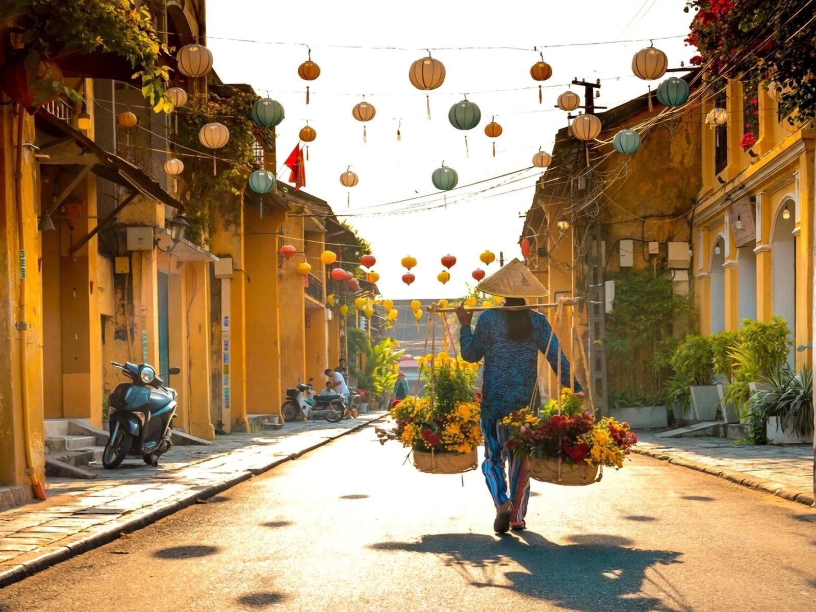 Person carrying flowers with lanterns overhead in Hoi An town