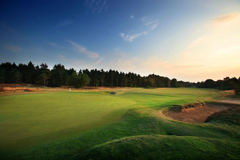 Sunset view of a green with trees bordering the fairway.