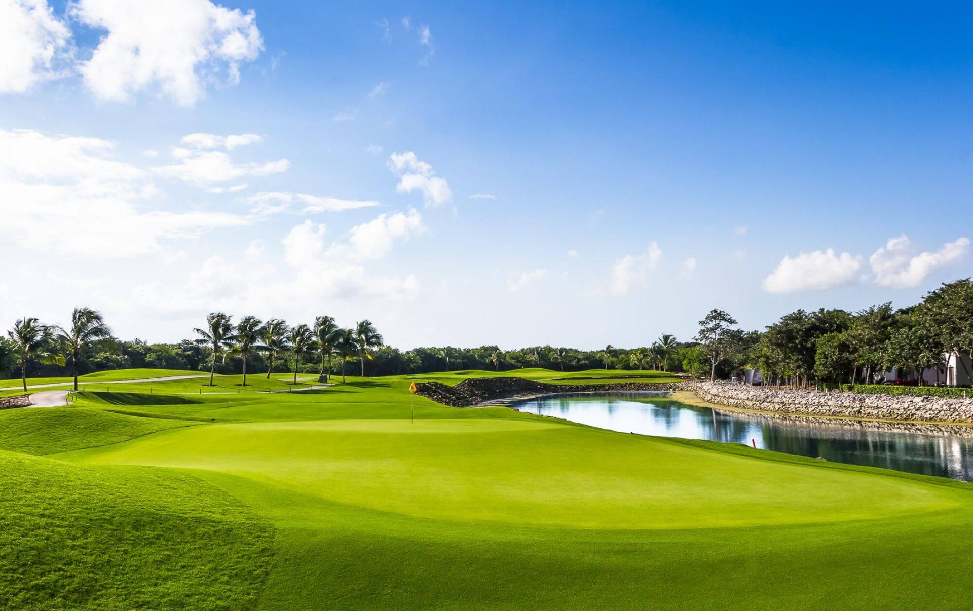 A wide fairway leading to a well-kept green elevated from the water hazard