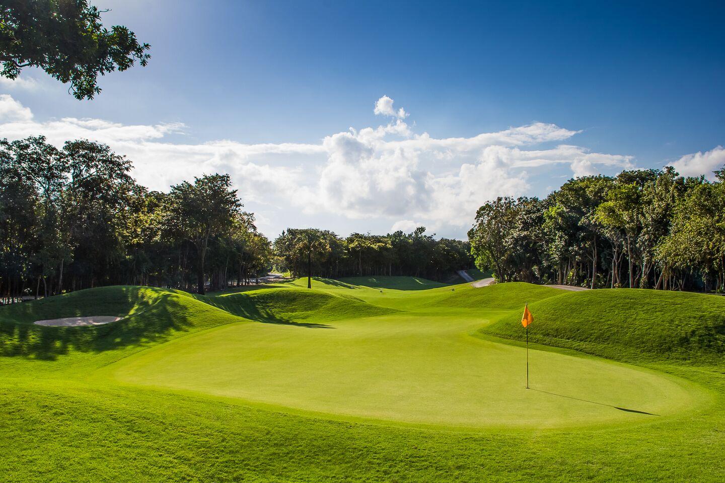 A well-maintained green surrounded by rolling dunes under cloudy blue skies