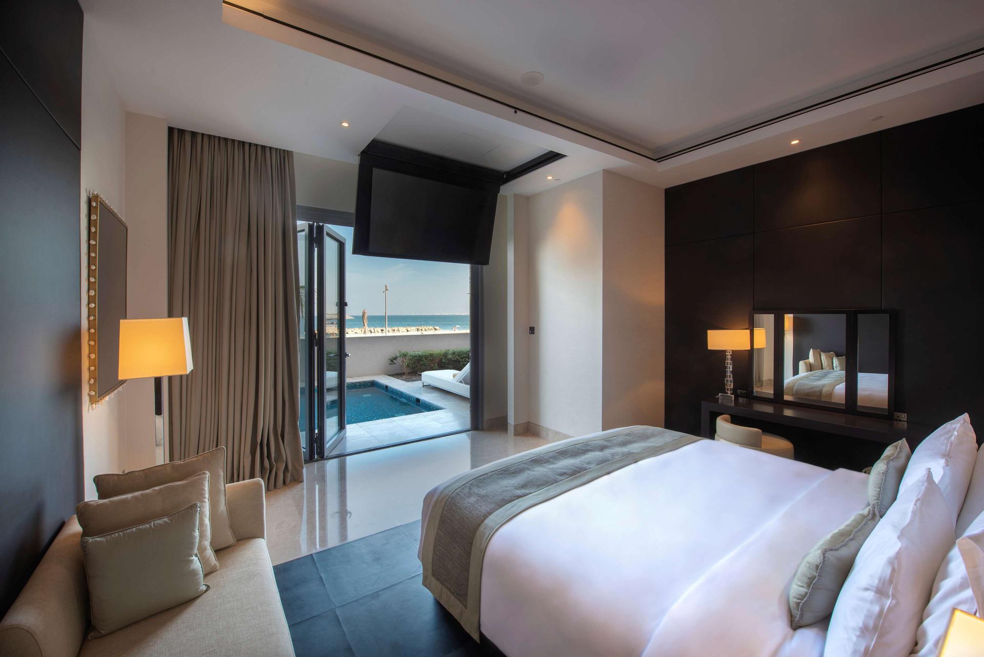 A double bed room with a TV hanging from the ceiling alongside a patio space a private pool and sunbed