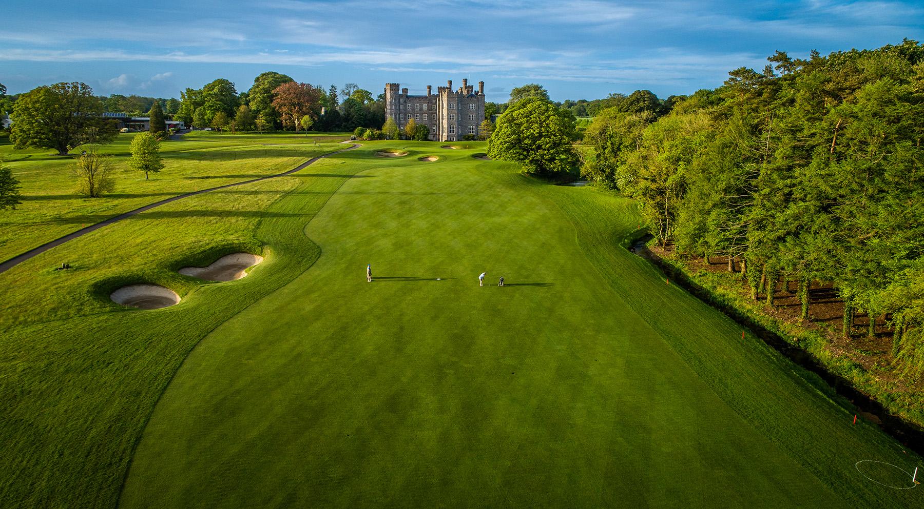 A fairway leads to a historic castle with two golfers playing.