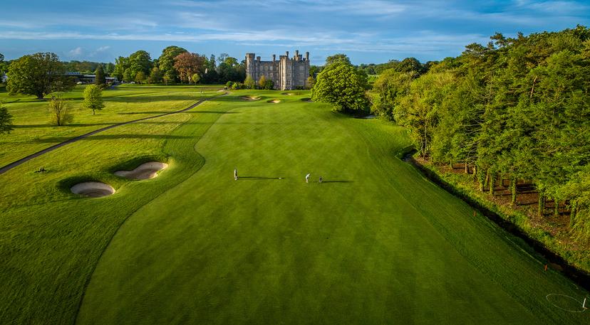 A fairway leads to a historic castle with two golfers playing.