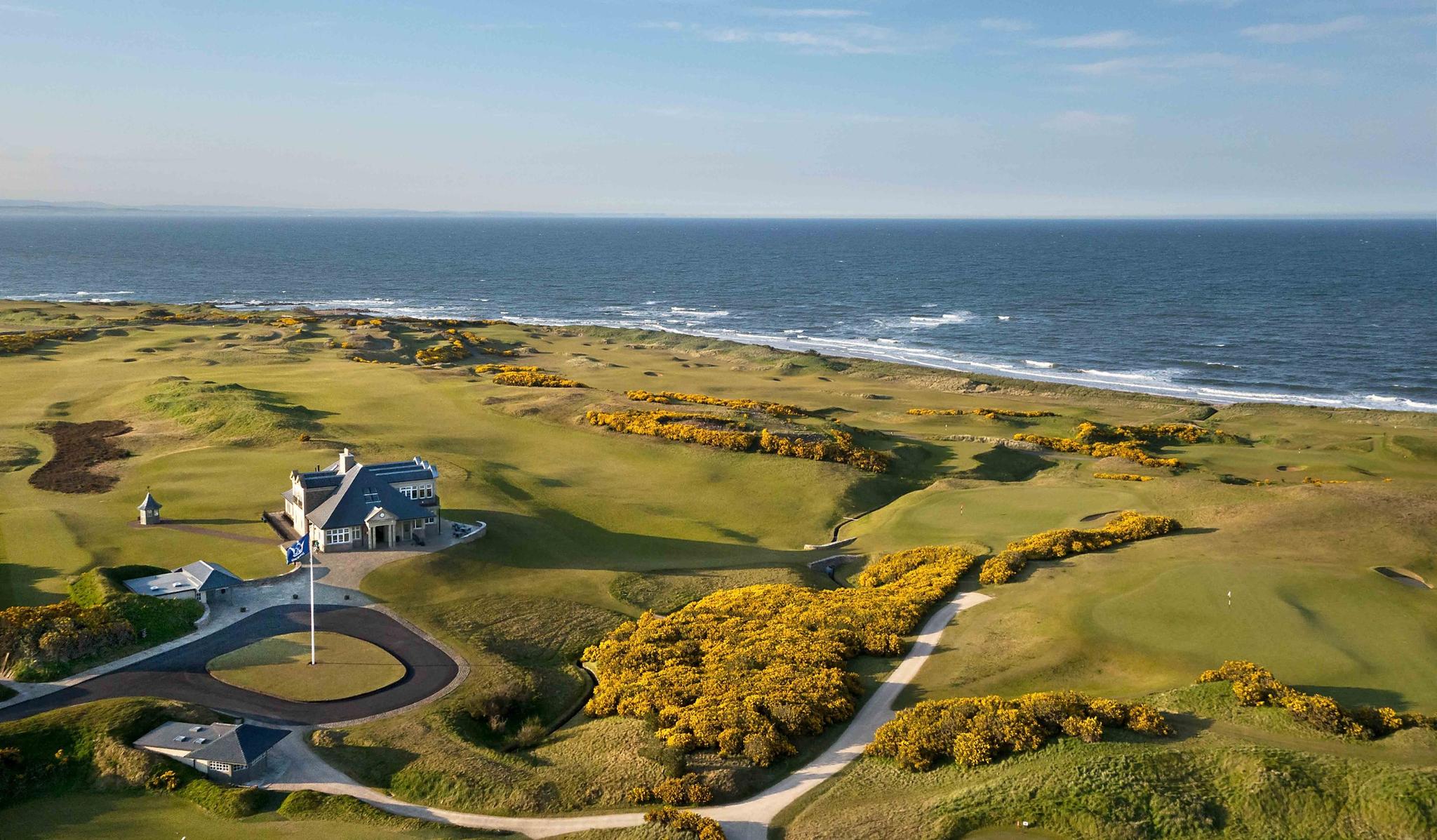 A panoramic view of the course with bright yellow gorse bushes contrasting the ocean backdrop.