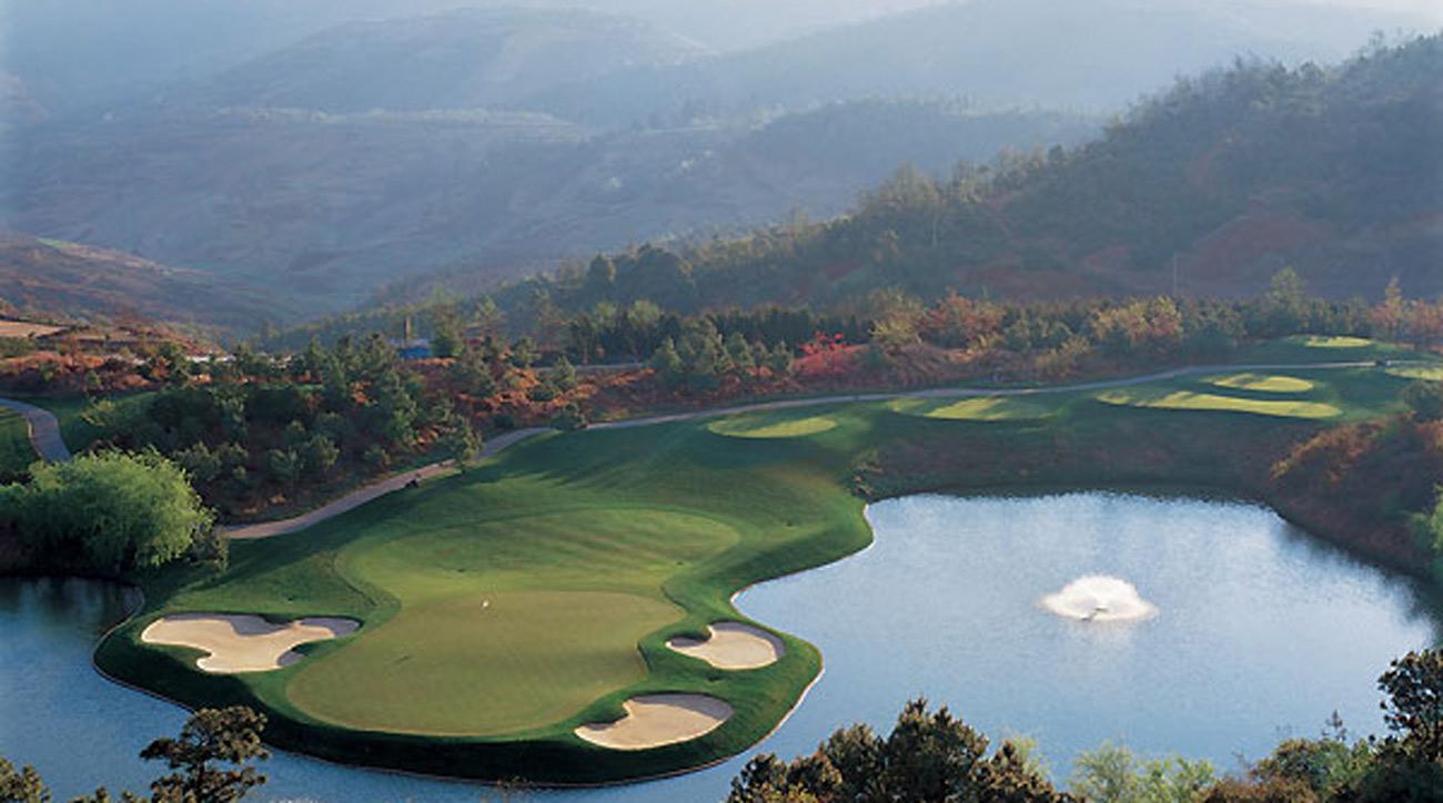 A beautiful golf green surrounded by water and mountains in the distance.