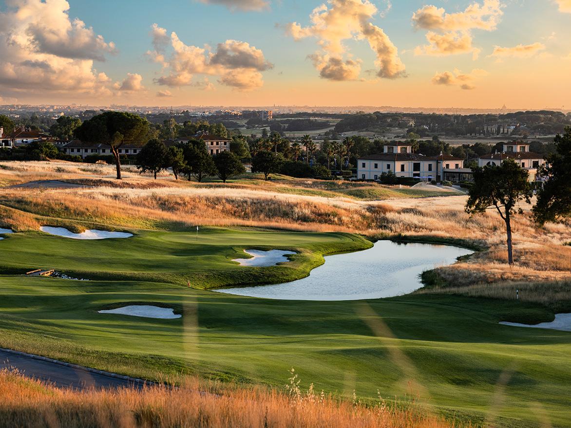 Sun setting over a smooth green surrounded by a yellow mature rough with city views