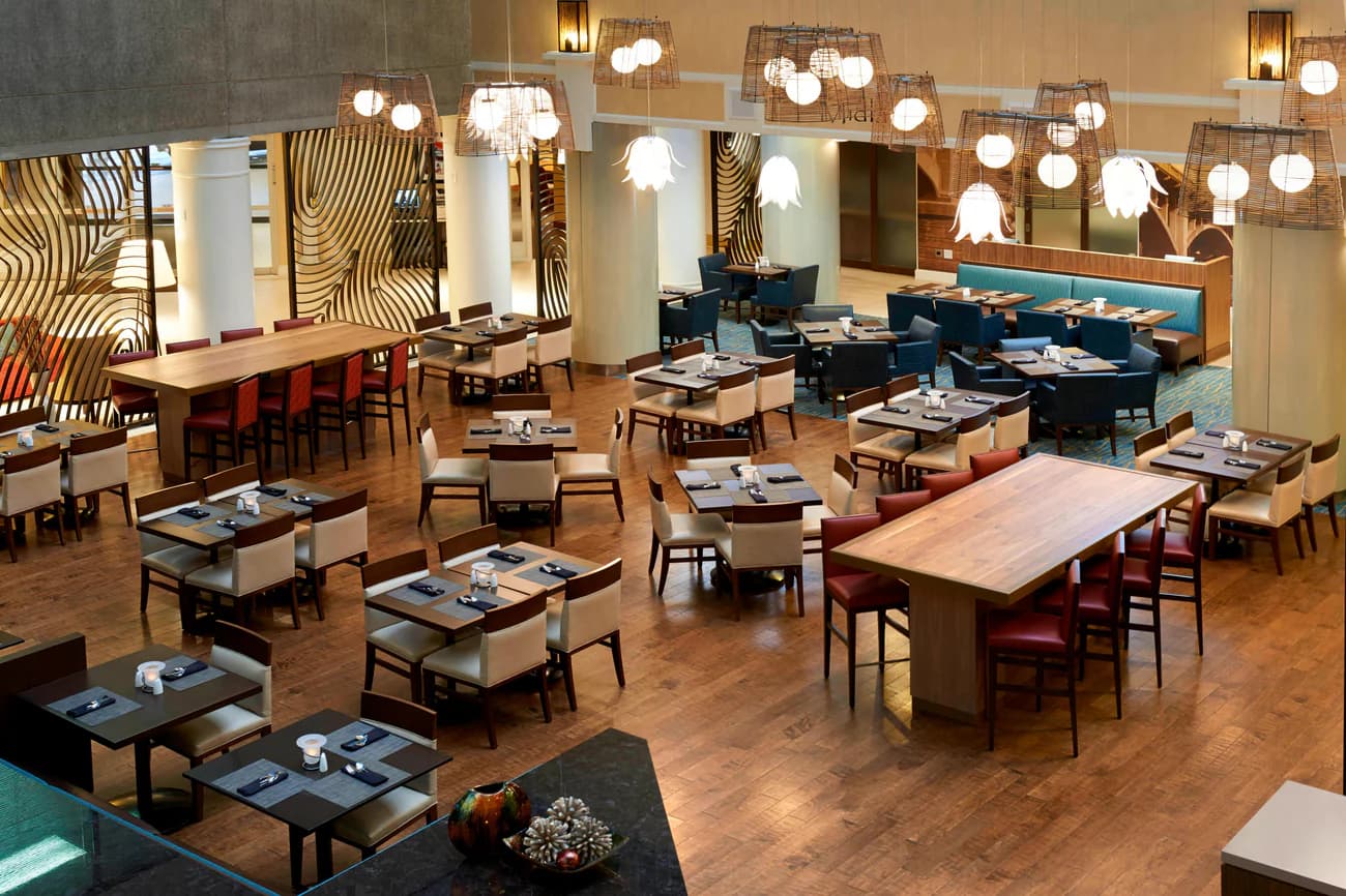 A contemporary hotel restaurant with wooden floors, stylish lighting, and neatly arranged tables.