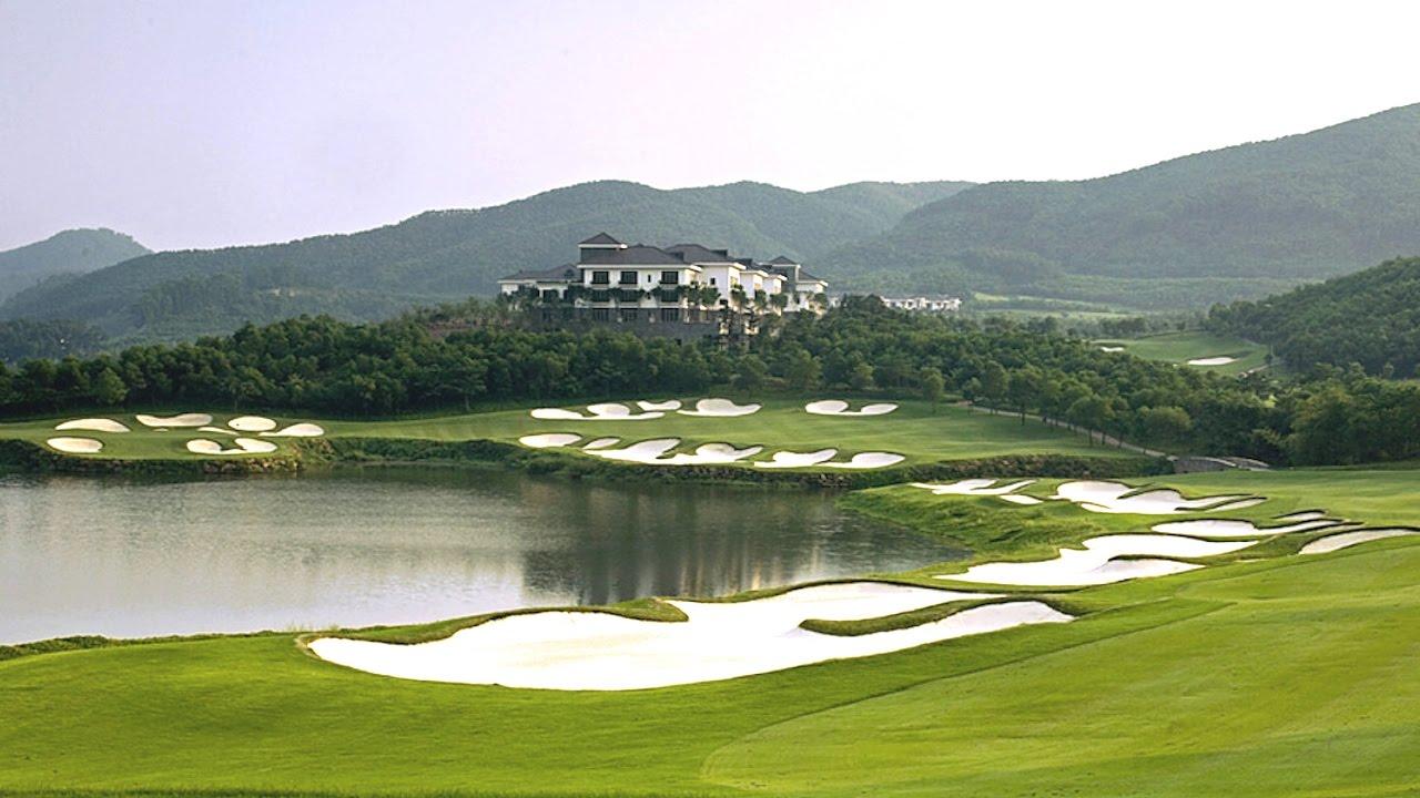 A scenic golf course with multiple bunkers around a lake and a clubhouse on a hill.