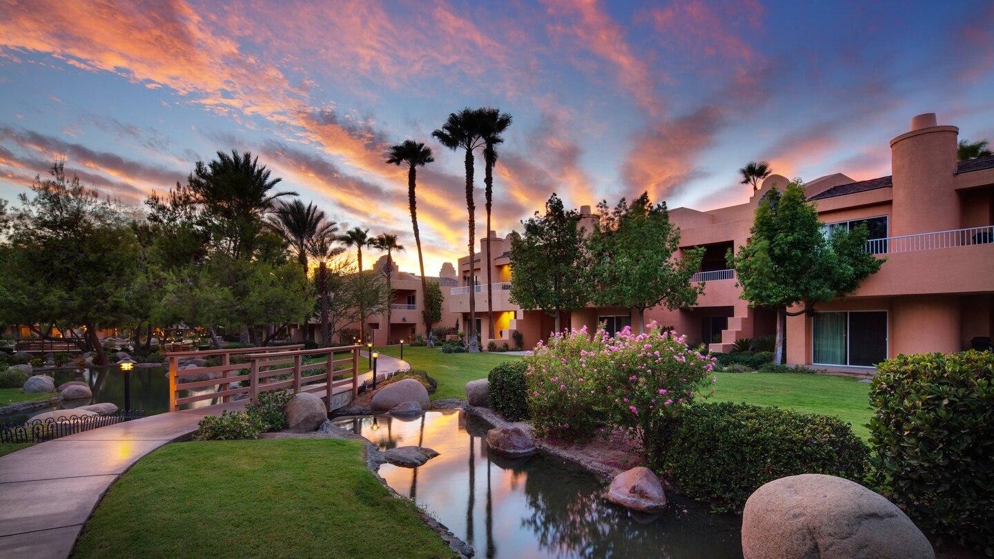 Garden at the resort with manicured brushes, palm trees, vibrant flowers and a wood bridge to navigate the resort's river.