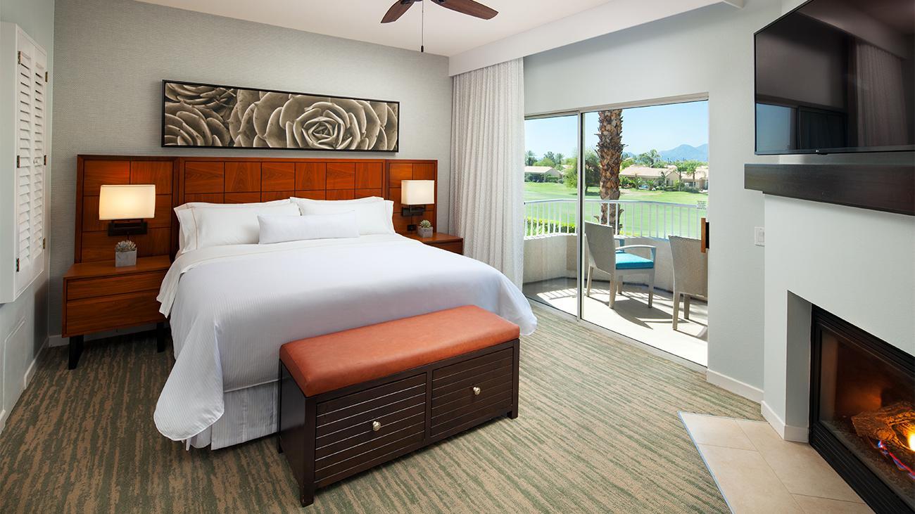 Modern double bed room at the Mission Hills Resort featuring a fireplace below the TV and balcony views of the course is distant mountains