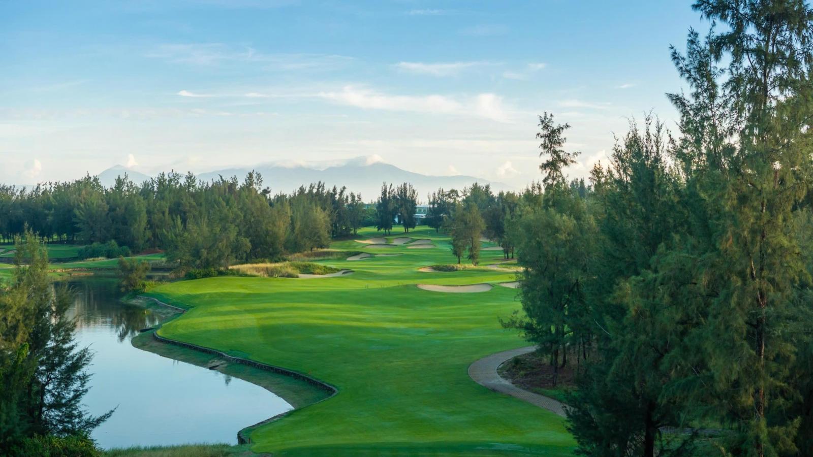 A lush golf course winding through tall trees and natural water features.
