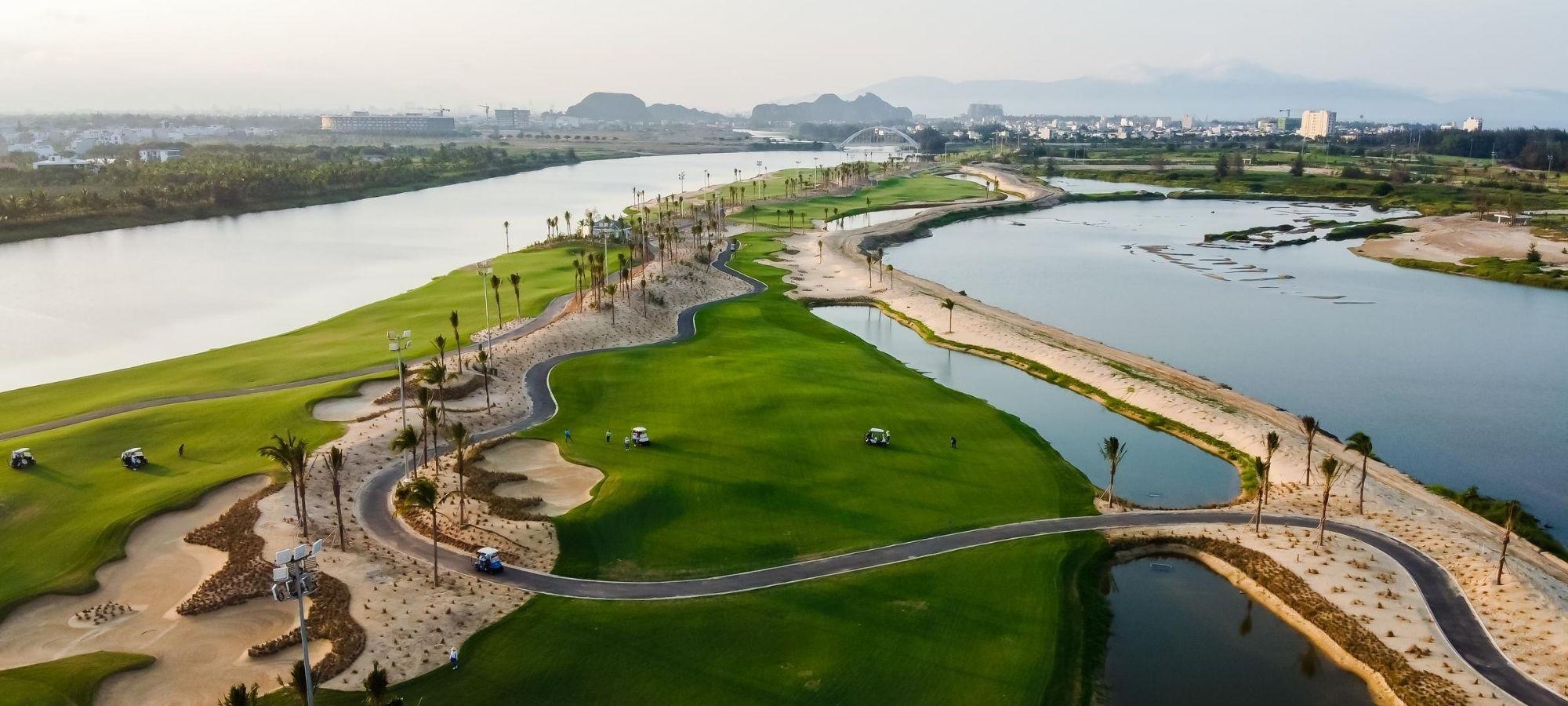 An aerial view of a riverside golf course with winding paths and sand traps.