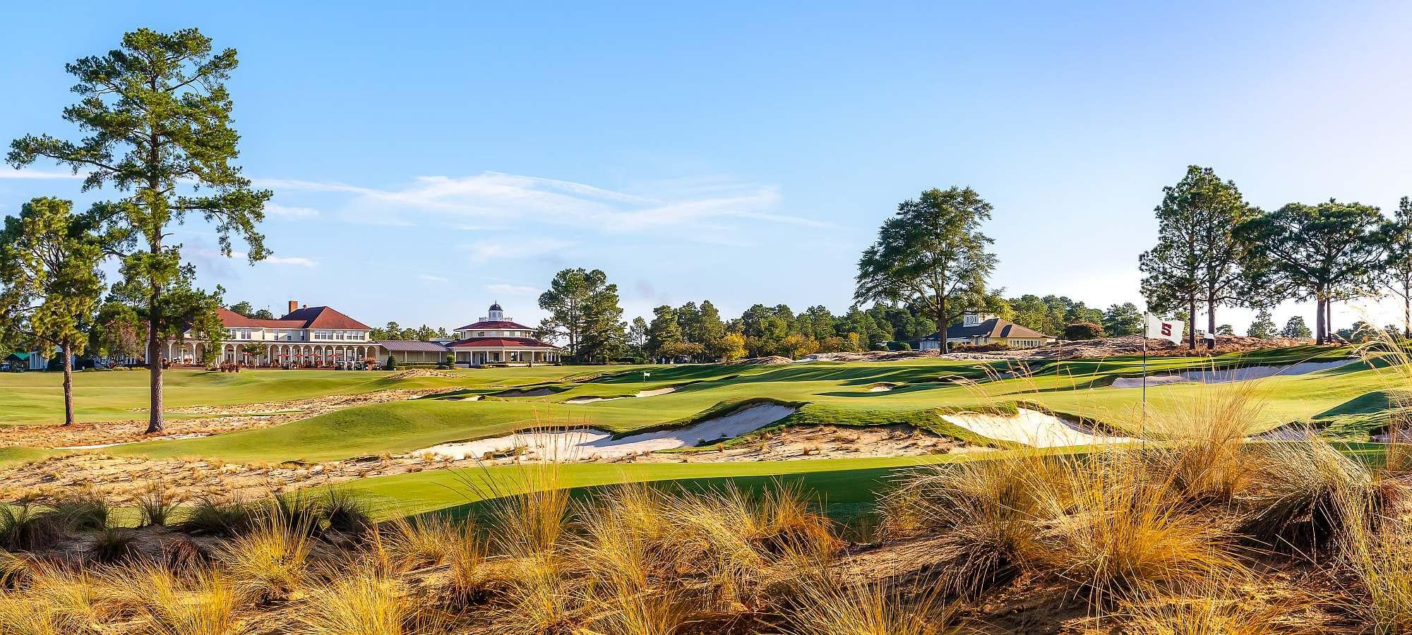 Panoramic view of the course littered with sand bunkers and the clubhouse overlooking under blue skies