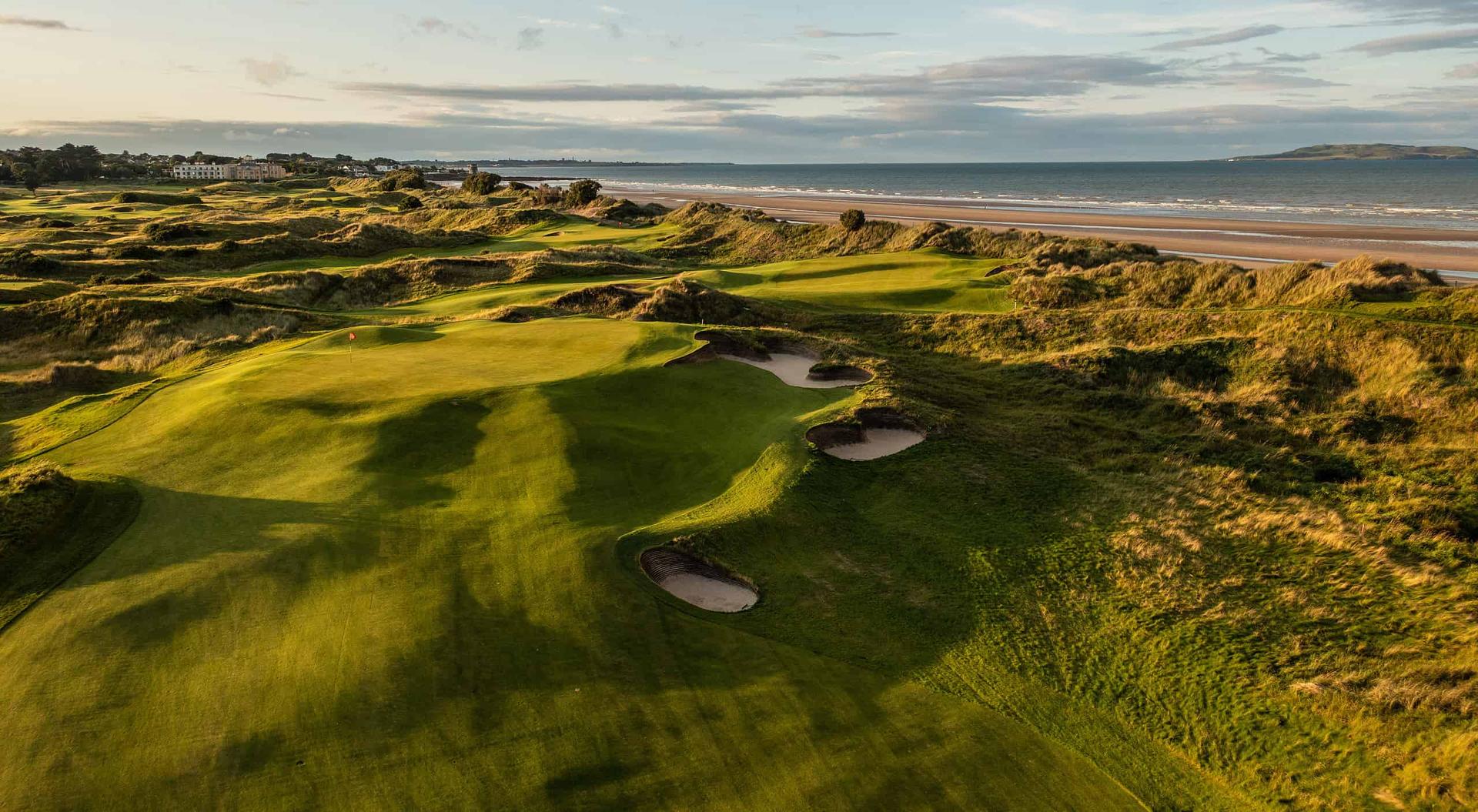 A golf green with bunkers overlooks the ocean and coastline.