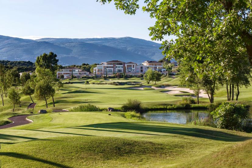Tee shot over water with bunkers on the right and the hotel and mountains in the background