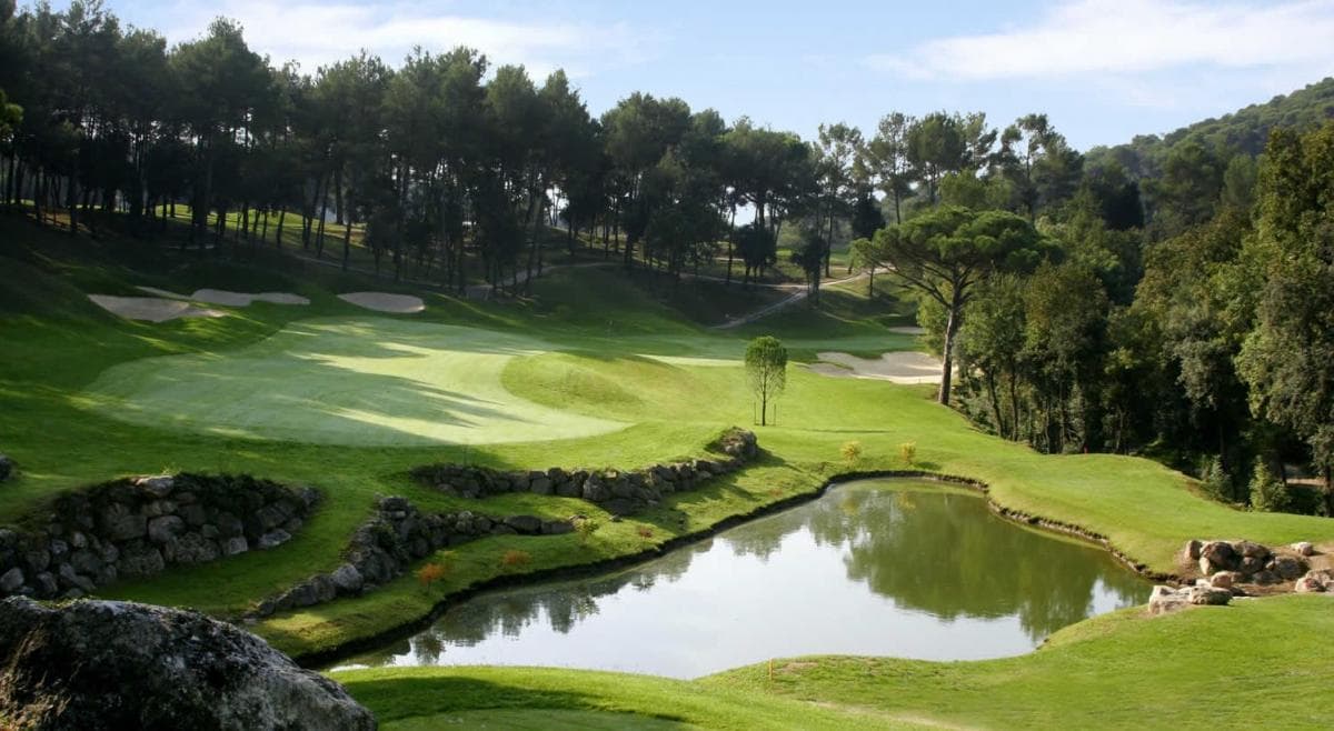 Water hazard in the foreground leading to a winding, narrow fairway lined by trees