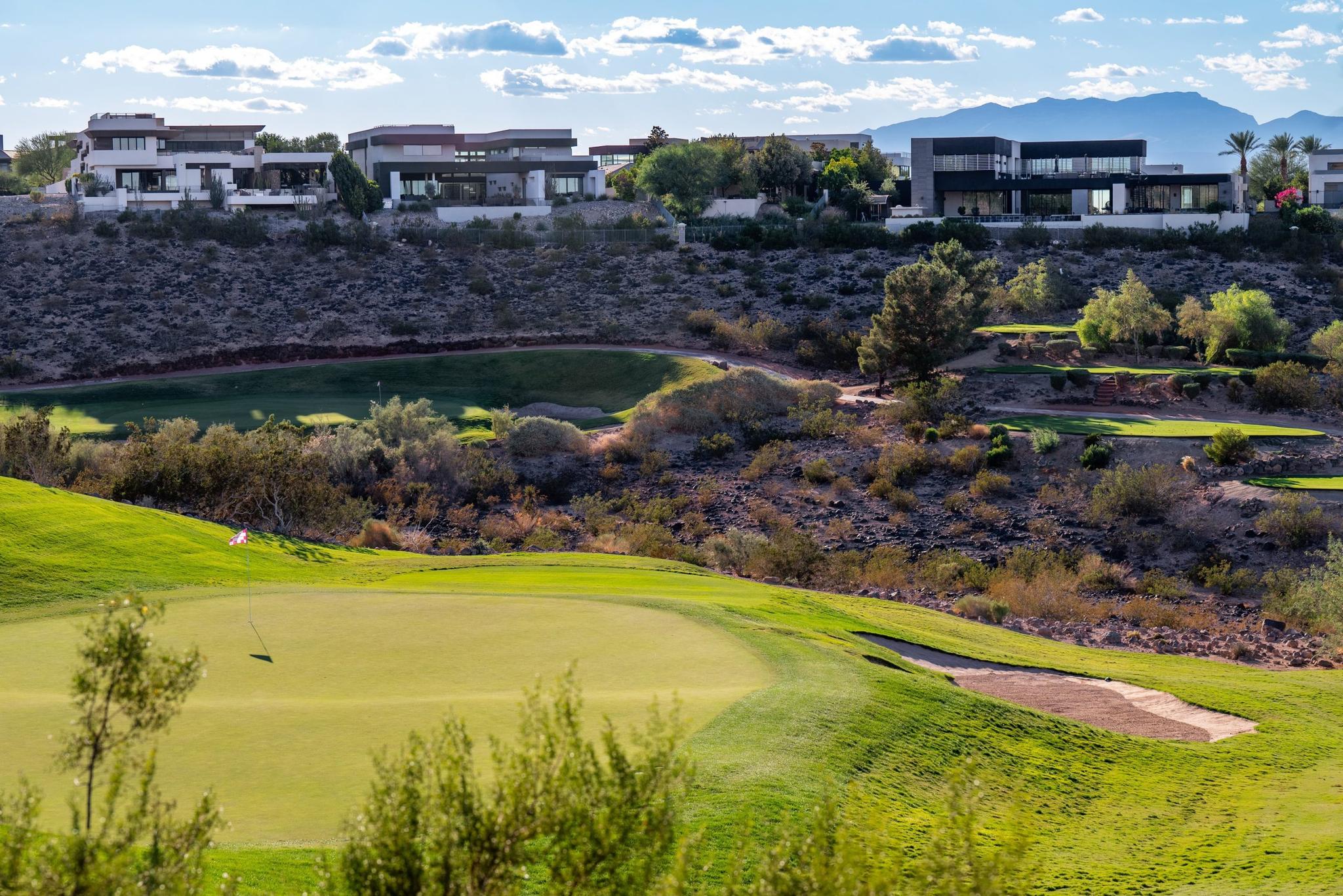 A pristine green at Serket Golf Club framed by desert terrain and luxury modern homes.