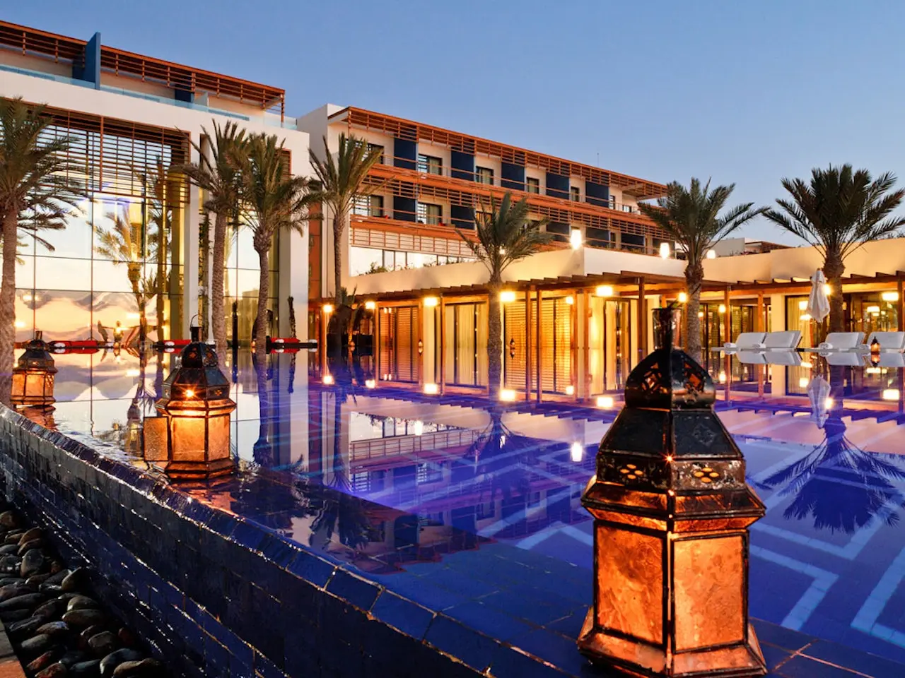 The swimming pool in the evening being lit up by the buildings lights and lamps