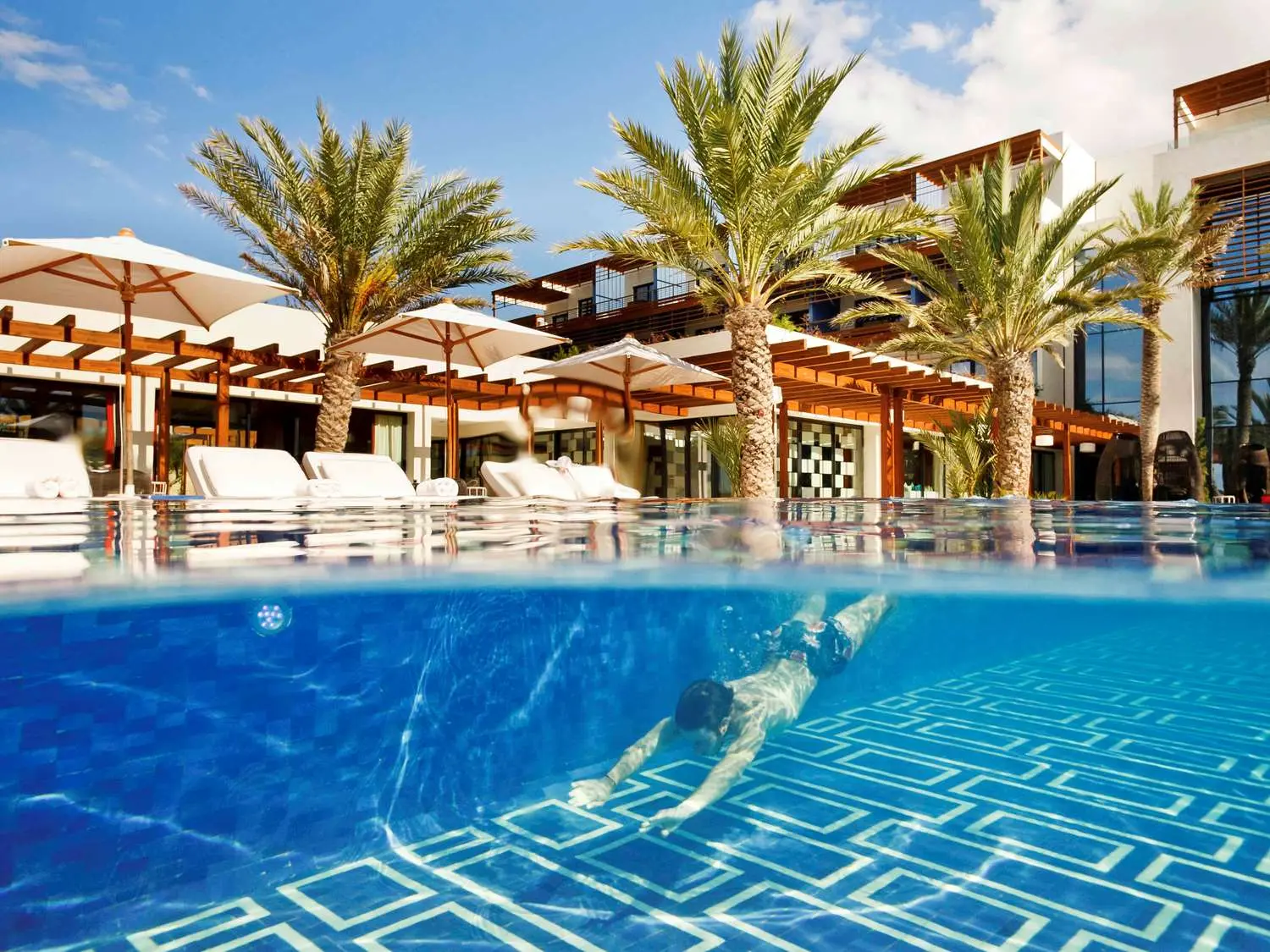Outdoor swimming pool nestled with sunbeds and palm trees